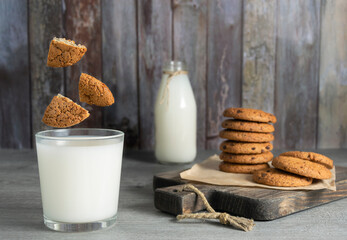 Pieces of oatmeal cookies fly into a glass of milk. Cookies are stacked on a wooden board