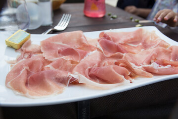 Prosciutto, an Italian dry-cured ham, thinly sliced and served uncooked in a white plate