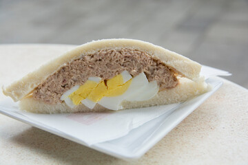 Close up of a Tramezzino, a triangular Italian sandwich constructed from two slices of soft white bread, with the crusts removed, containing hard boiled egg and tuba fish 