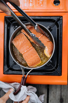 Crop person frying salmon on tourist stove