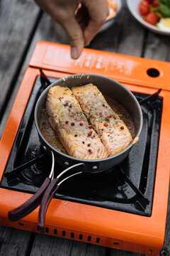 Person peppering salmon in pan on camping stove 