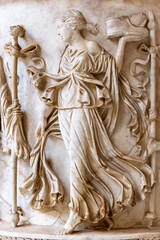 Close-up on decorative sculptures engraved on a marble wall representing a woman in a beautiful dress carrying a shoe on the palm of her hand