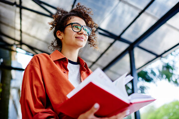 Positive ethnic female student with notebook on street