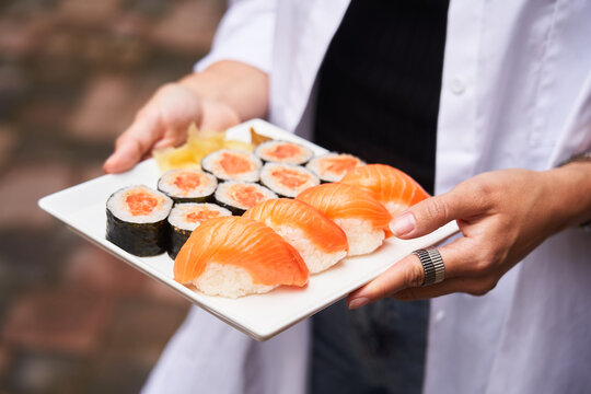 Crop young woman holding plate of sushi