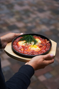 Crop young woman holding plate of shakshuka