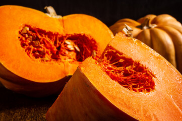 Whole fresh orange big pumpkin and slice of pumpkin on black background, closeup. Organic agricultural product, ingredients for cooking, healthy food vegan.