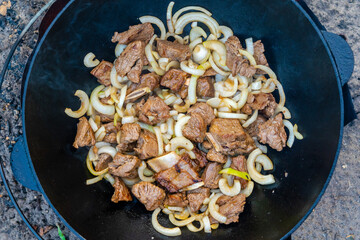 Process of cooking of delicious pilaf - fried meat with onion in a cauldron outdoor