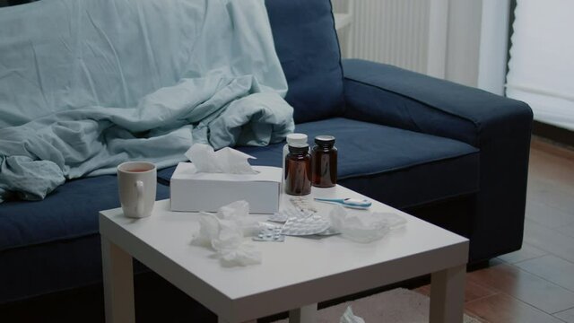 Close up of medicaments and thermometer on coffee table with nobody in room. Empty place with medicine against flu, bottles of pills, drugs, medication, cup of tea and tissues for treatment