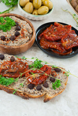 Sun dried tomato with a slice of bread with hummus and a plate of olives