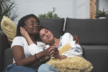 Two young mixed race lesbian couple black African and white woman sitting in their apartment and...
