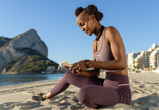 Black sportswoman using smartphone on beach