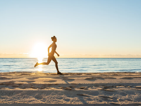 Unrecognizable sportswoman running against rising sun