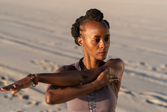 Black sportswoman stretching arms on beach