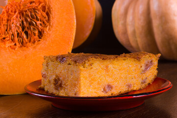 Homemade pumpkin pie for Thanksgiving on a red saucer, and a large fresh sliced orange pumpkin, wooden background, close-up. Organic agricultural product, cooking, healthy vegan food.