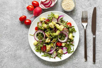 Vegan salad with red onion, tomatoes, avocado and radish on grey background, top view