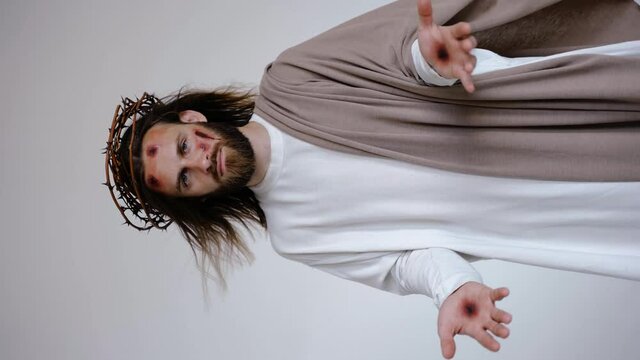 Jesus with wounds on his head and stigmata on his hands looks at the camera on a white background. Studio. High quality 4k footage
