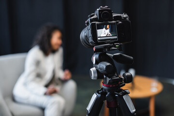 modern digital camera on tripod with african american journalist sitting in armchair on screen