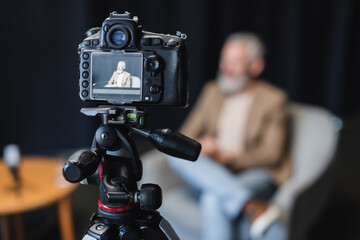 modern digital camera on tripod with businessman sitting in armchair on screen