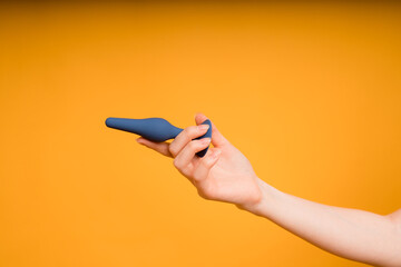 A blue butt plug lies in a woman's hand on an orange background.Useful for a sex shop