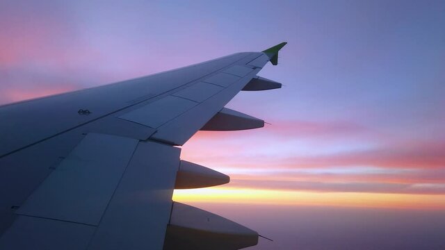 The view from the window of the plane on the silhouette of the wing and the setting sun. Blue, burgundy clouds in the sun.