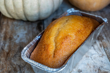 Pumpkin sponge cake in a freshly baked aluminum container, on a rustic wooden background, decorated with natural pumpkins.