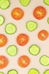 On the pink background of the vertical photo there are round slices of green cucumber and red tomato