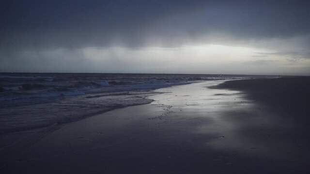 Orilla de la playa un d&iacute;a de mal tiempo con nubes negras precipitando lluvia en el horizonte