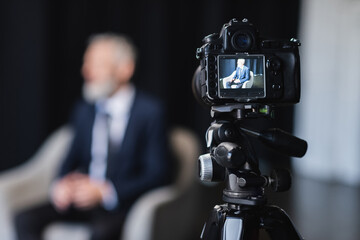 digital camera with businessman in suit sitting in grey armchair during interview on screen - obrazy, fototapety, plakaty