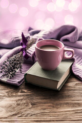 Morning coffee. A cup of coffee on a book and a warm sweater on a wooden table against the background of a bouquet of lavender.Beautiful bokeh. Still life concept. Copy space. 