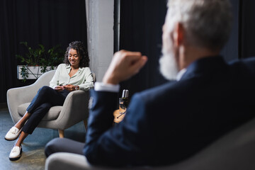 happy african american journalist smiling near blurred businessman during talk show