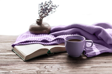 Morning coffee. A cup of coffee on a wooden table, an open book and a warm sweater on the background of a bouquet of lavender. Still life in lavender color. Cozy morning. Copy space.