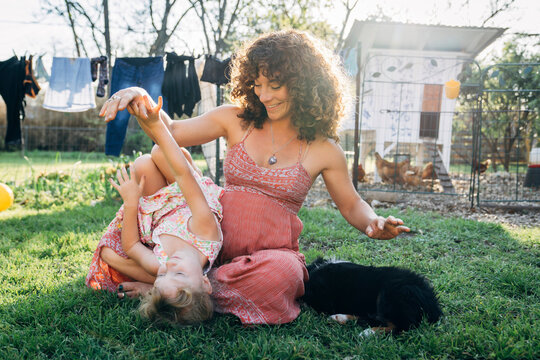 Pregnant woman sitting in grass in yard tickling laughing daughter