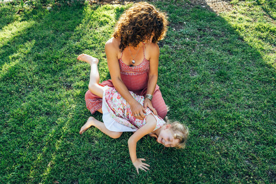 Pregnant woman sitting in grass in yard tickling laughing daughter