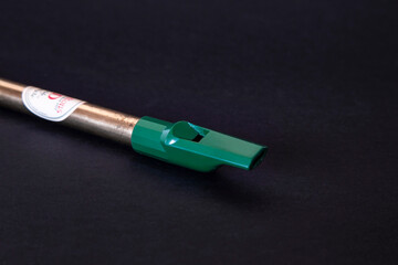 Tin whistle, brass and green over black background. Close up photography