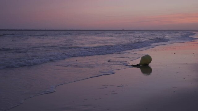 Playa al atardecer con la marea baja y una boya en ll orilla