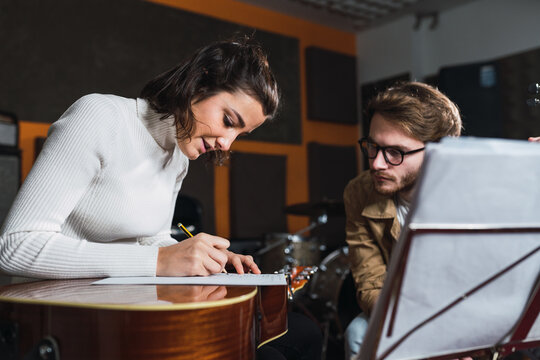 Woman with guitar writing on paper near man in studio