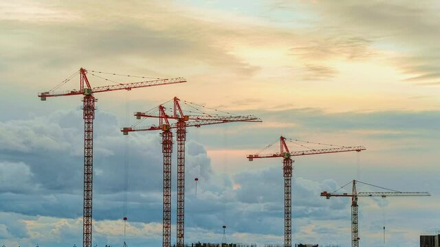 Timelapse of construction cranes working on a construction site in the evening against the background of clouds, Workers are building a residential building.
