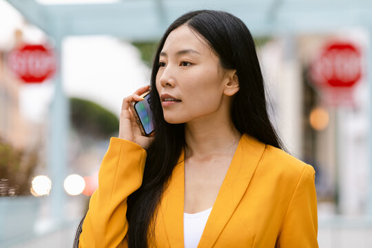 Young Chinese businesswoman speaking on smartphone on street