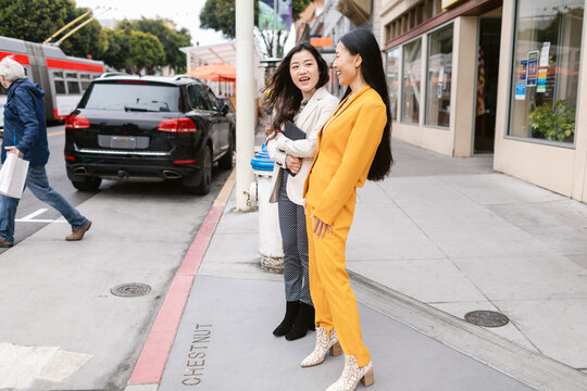 Cheerful stylish girlfriends talking on street
