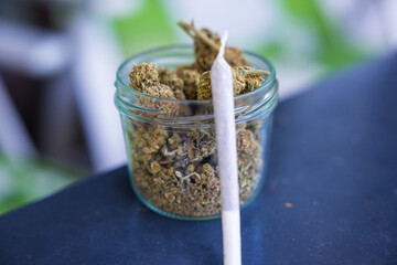 Closeup shot of dry marijuana cannabis buds in a jar with a rolled blunt leaned on it.