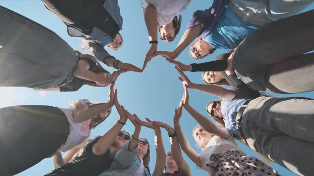 Cheerful girlfriends make a heart shape out of their hands.