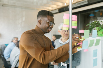 Colleagues writing notes on a stickers on a glass wall