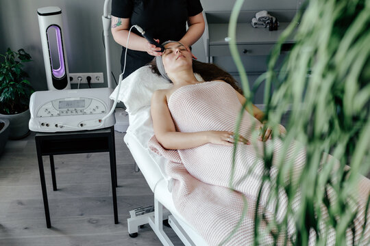 Crop female beautician doing ultrasonic massage to woman