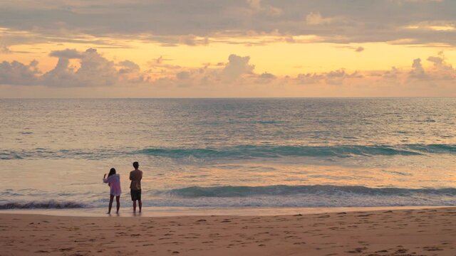 Full shot from behind of unknow couple watching sunset beach. Romantic scene man and woman stay together with carefree.