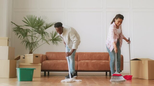 Relocation cleaning. Young cheerful african american amd and woman wiping and washing floor in new apartment together