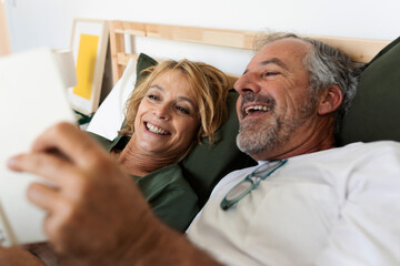 Joyful senior couple reading a book together on the bed