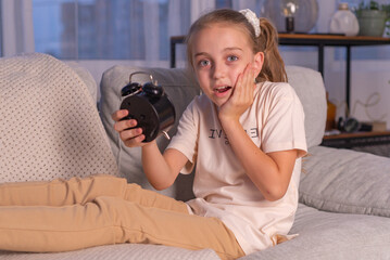 Little girl sleeping in bed with alarm clock on the table. Wake up early in the morning. We put the...