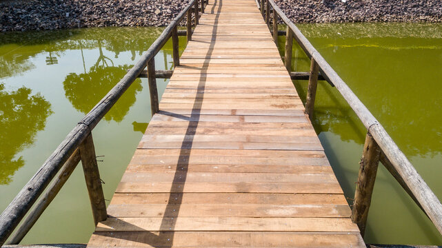 Wooden bridge, with handrail, in a lake with greenish water, in drone image