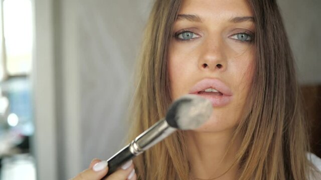 a young and beautiful girl blows powder from the brush directly into the camera. Girl with clean and beautiful skin. High quality FullHD footage