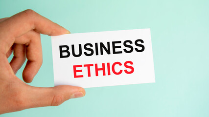 businessman's hand holding paper business card with text business ethics, closeup light blue background